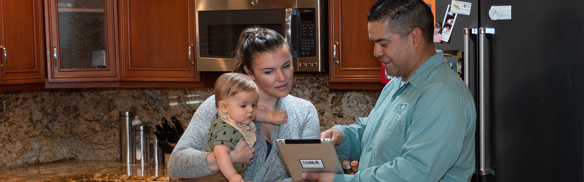 Image of a homeowner holding her baby while speaking with AIPM technician and looking at tablet.